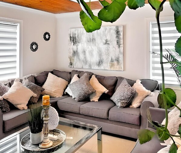 A modern living room with a grey sofa, decorative pillows, a glass coffee table, and a large abstract painting on the wall. - Chic Ocean Miami 88 (Cutler Bay)