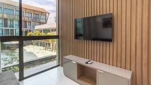 A modern living room with a large TV mounted on a wooden wall, a glass door leading to an outdoor area, and a minimalist furniture design. - Sunny Hall Flat by EasyHome (Ipojuca)