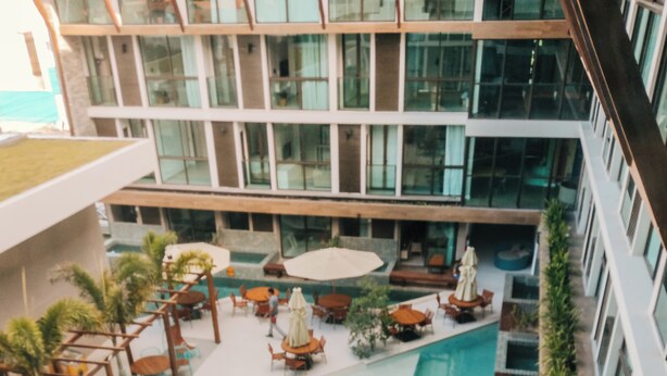 A modern hotel with a central swimming pool, outdoor seating areas, and a view of the building's interior. - Sunny Hall Flat by EasyHome (Ipojuca)