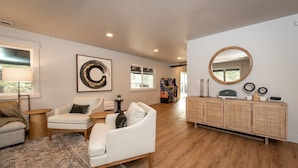 A spacious living room with a white sofa, a small round table, and a rattan console with decorative items.
