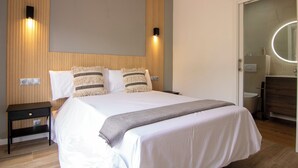 A bedroom with a bed, bedside tables, a wall-mounted light, and a bathroom visible through an open door. - Casa Rural La Lagunilla Golf (Candeleda)