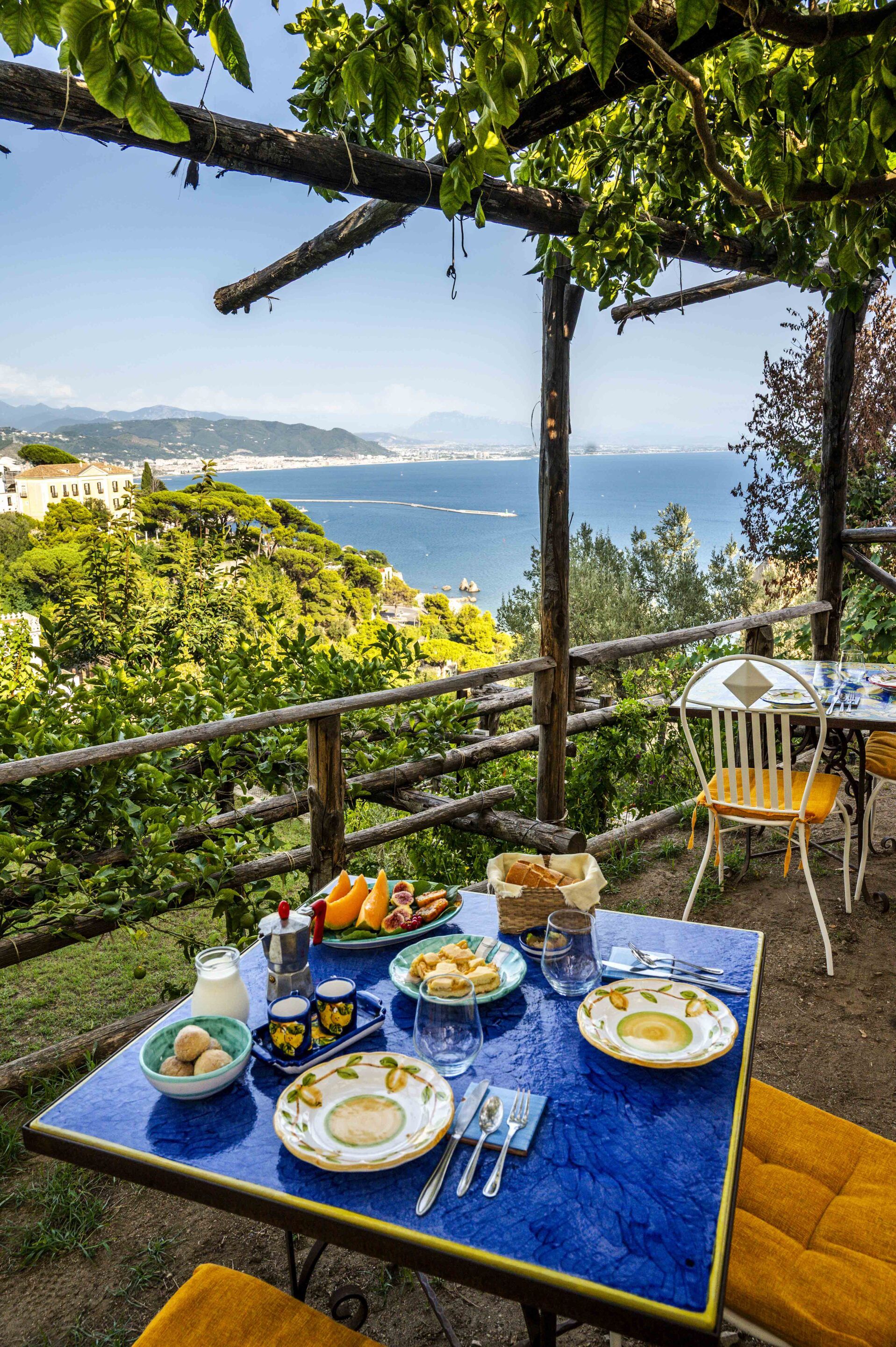 Un área de comedor al aire libre con una mesa lista para una comida, con vistas a un paisaje costero.