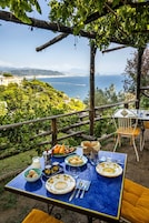 Un área de comedor al aire libre con una mesa lista para una comida, con vistas a un paisaje costero.