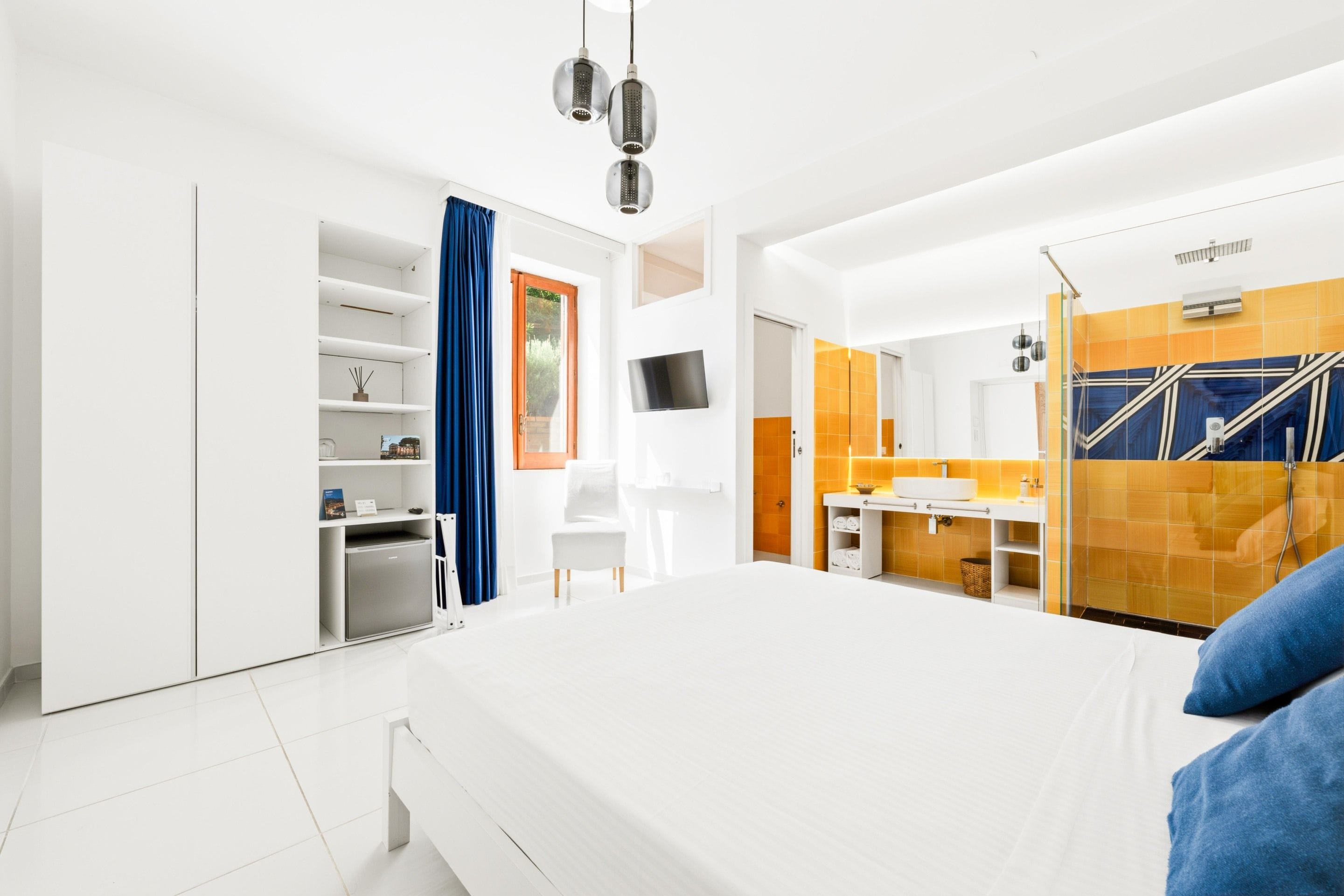 Una habitación de hotel moderna con una cama grande, un escritorio, televisión y baño con espejo y ducha.