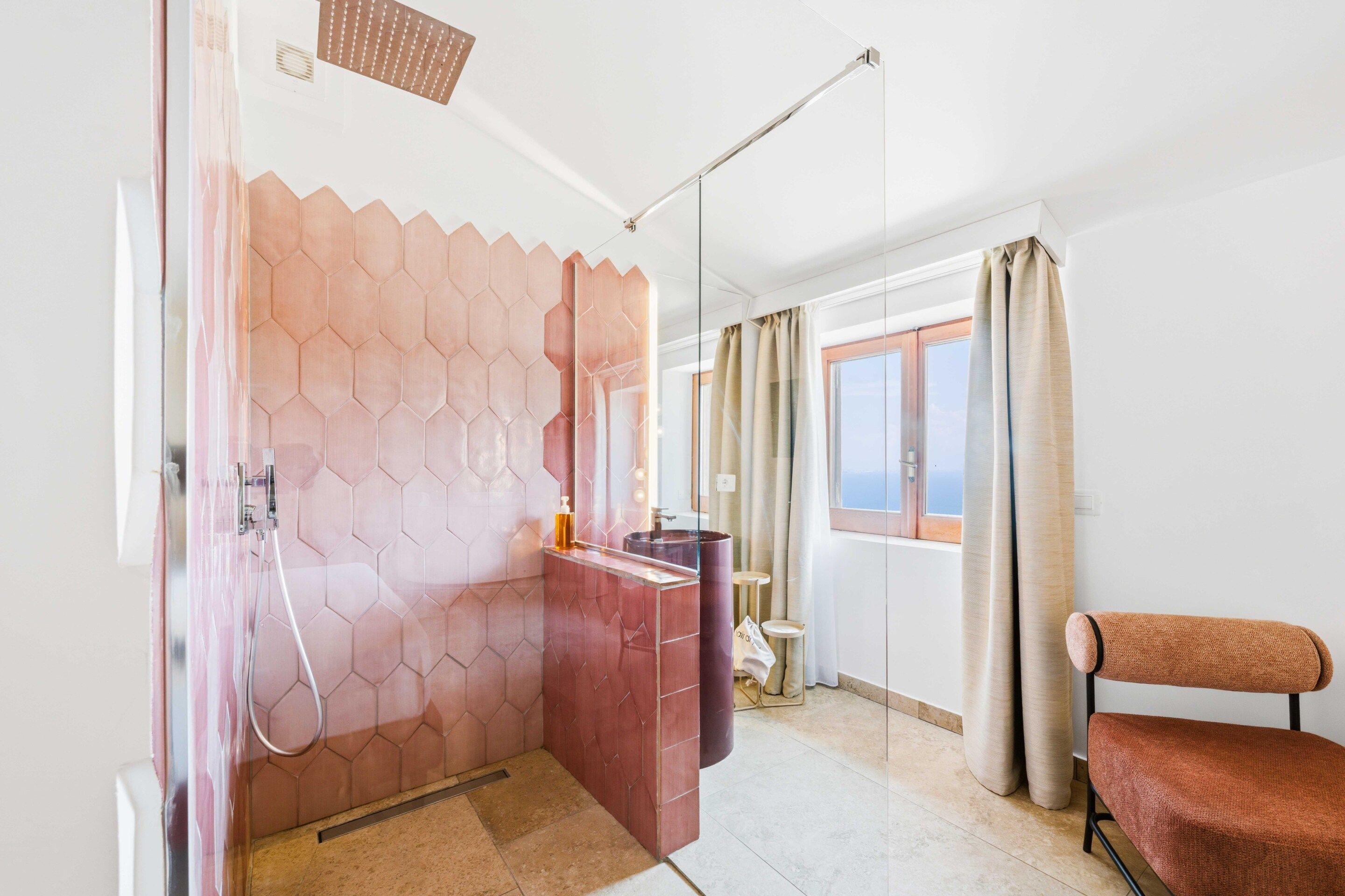 A modern bathroom with a shower, a vanity, and a view of the sea.