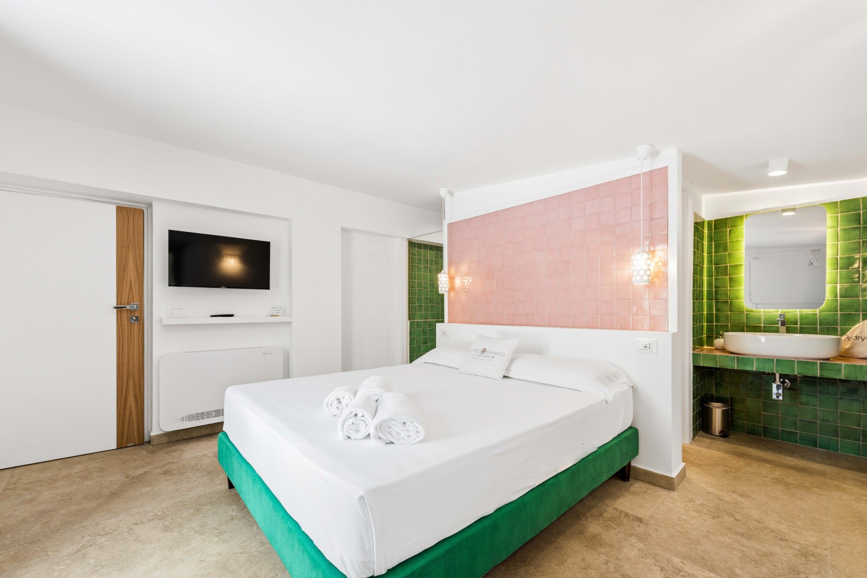 A hotel room with a bed, a television, a bathroom with a green-tiled wall, and a sink.