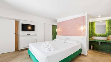 A hotel room with a bed, a television, a bathroom with a green-tiled wall, and a sink.