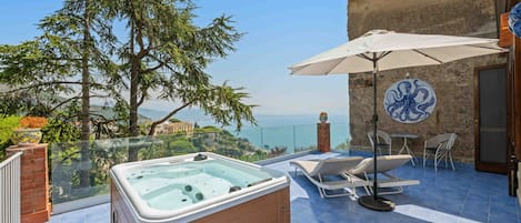 A rooftop terrace with a hot tub, lounge chairs, and a view of the sea.