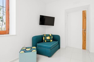 Una habitación con un sofá color turquesa, un reposapiés a juego, un televisor de pantalla plana montado en la pared y una puerta de madera.
