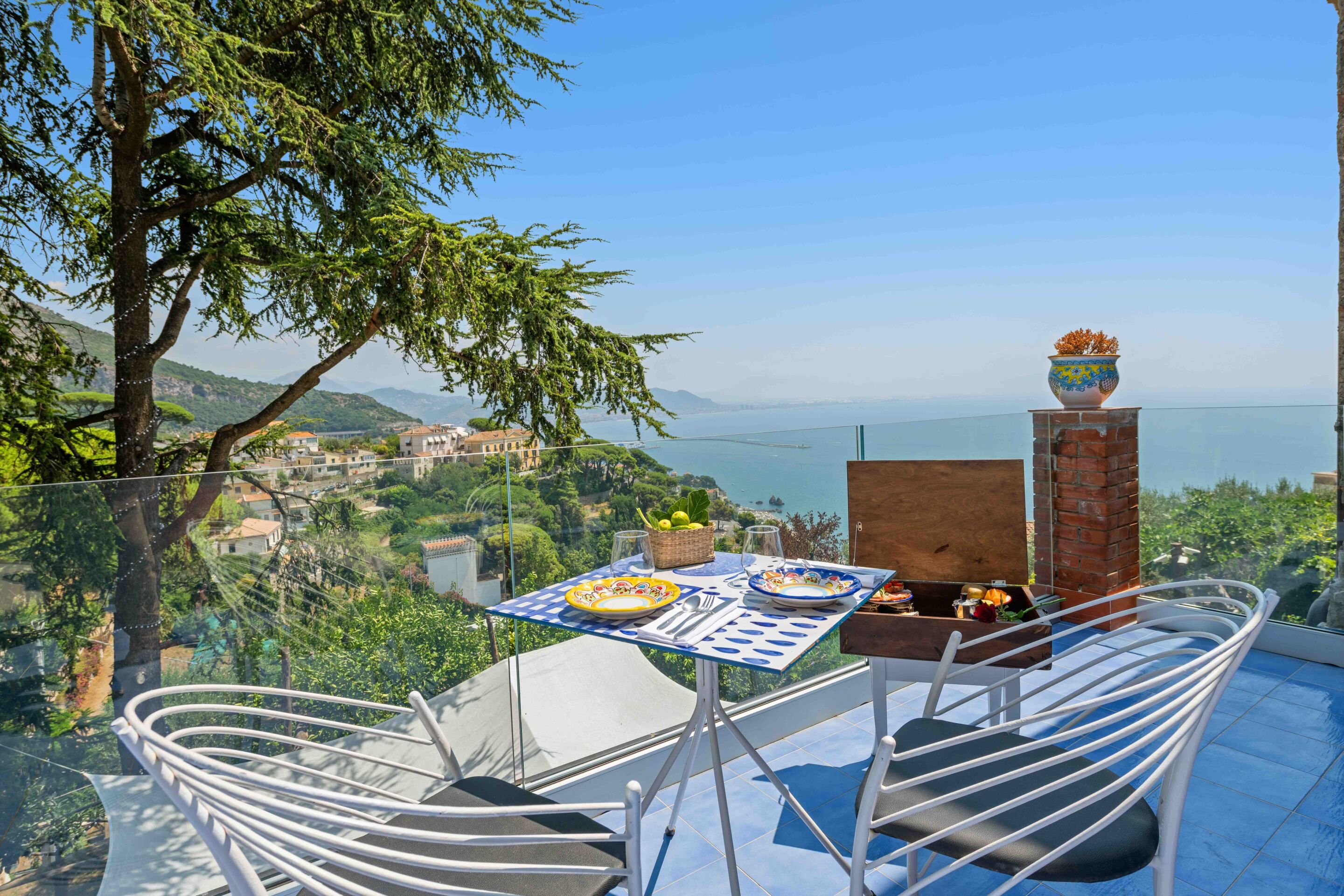 A terrace with a table set for dining, overlooking a coastal landscape.