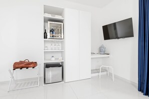A hotel room with a minibar, a television, a small table with a decorative item, a chair, and a luggage rack.