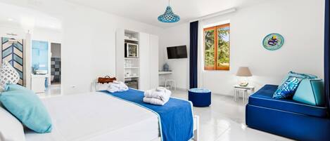A modern hotel room with a large bed, a sofa, a TV, and a window with a view of trees.