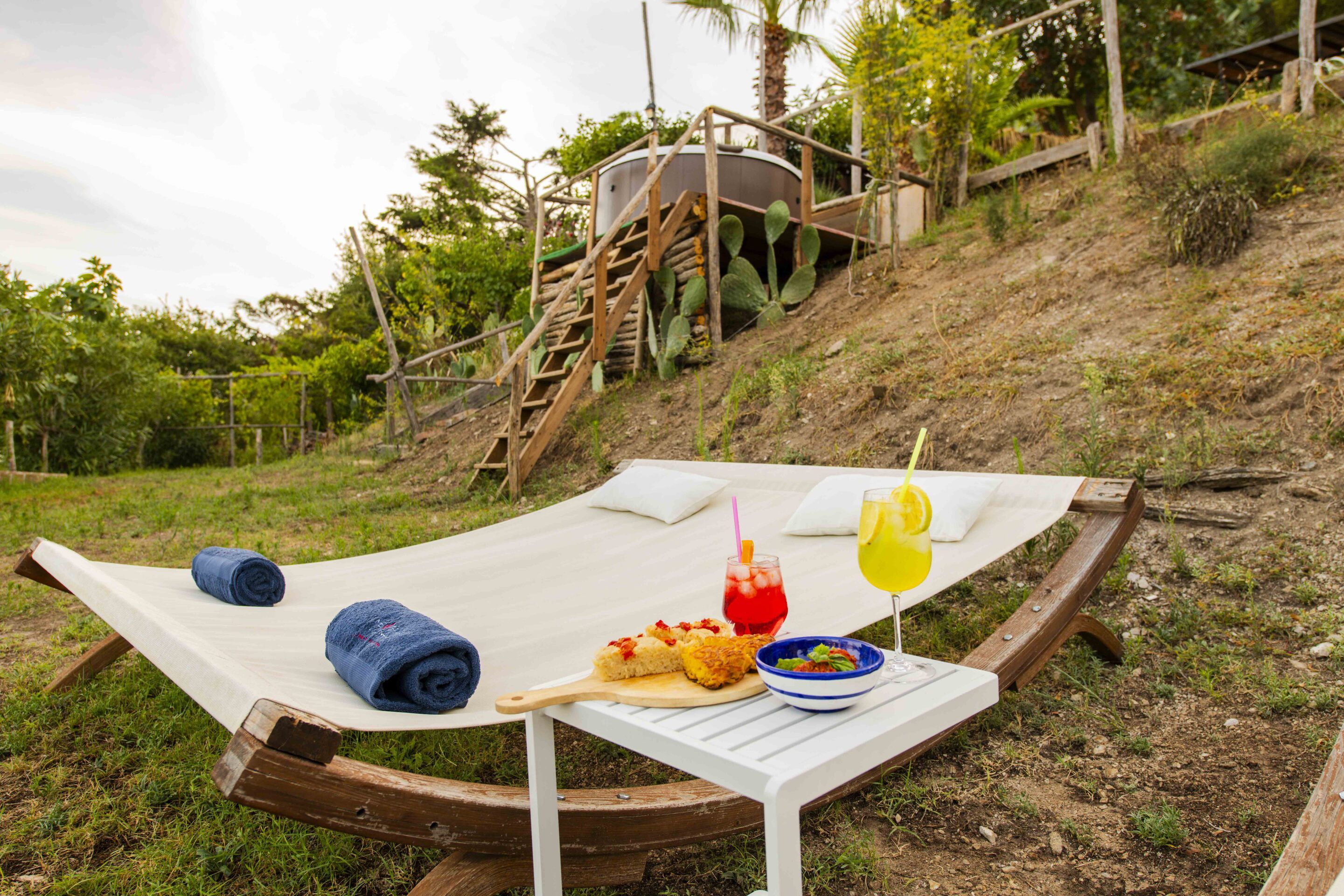 A hammock with a picnic setup including food, drinks, and towels.