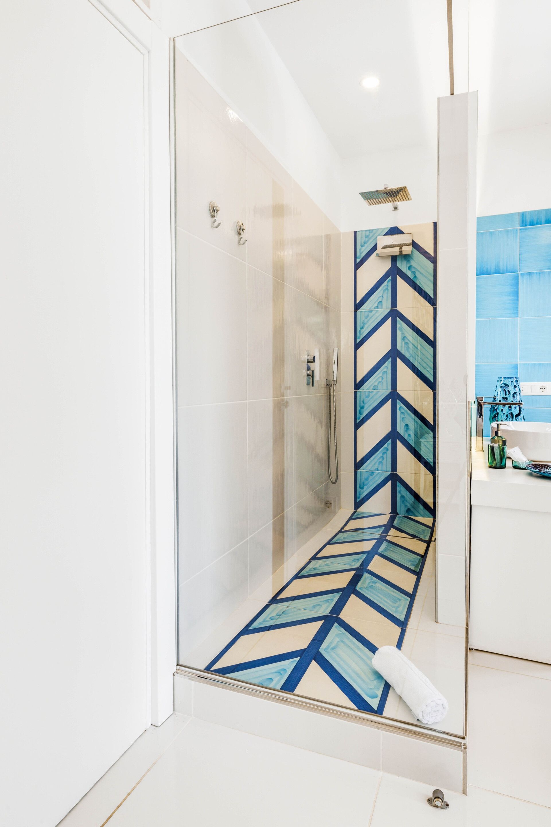 Un baño moderno con cabina de ducha de vidrio, suelo estampado y zona de lavamanos blanca.