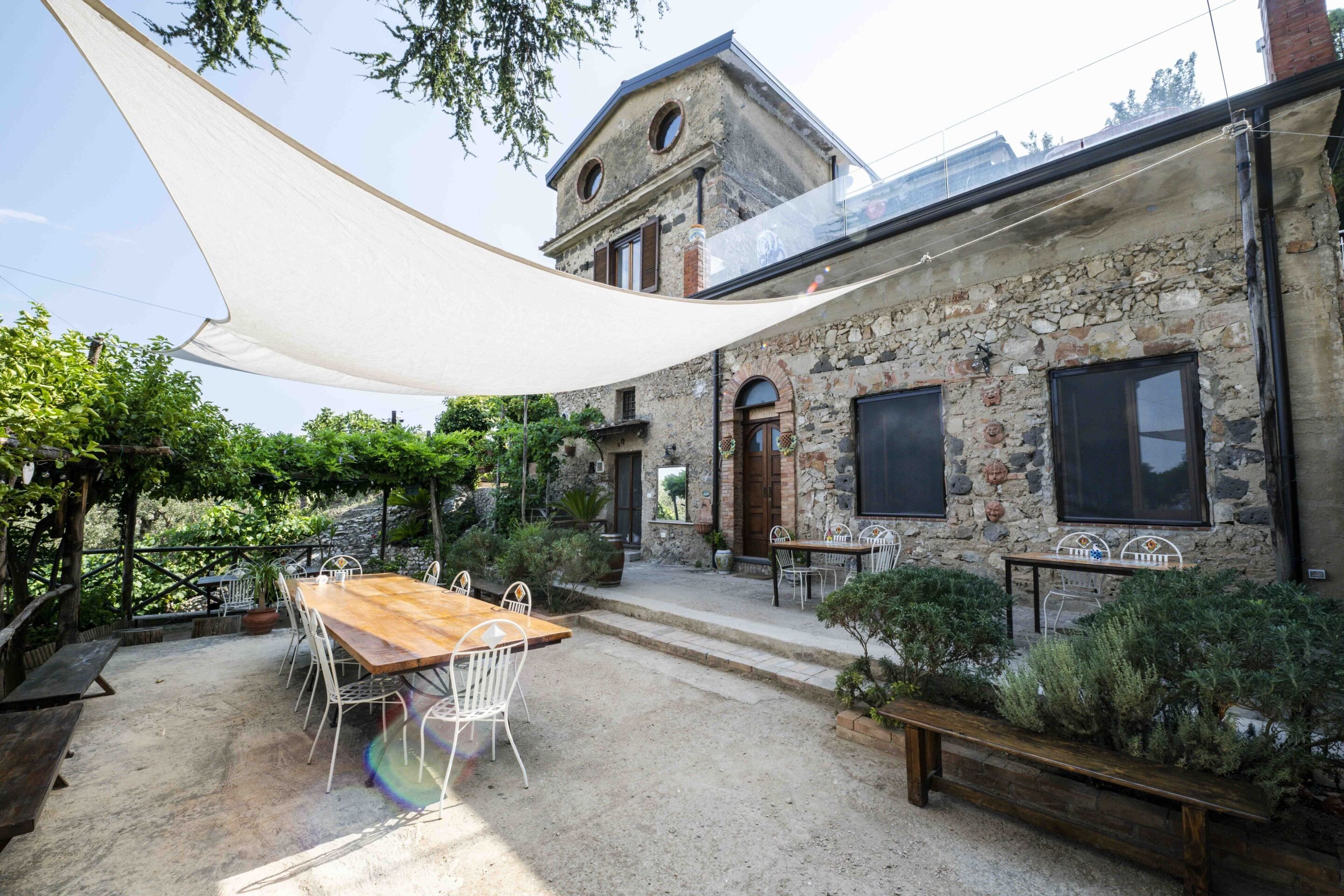 Un edificio rústico de piedra con una mesa y sillas de madera en el patio.