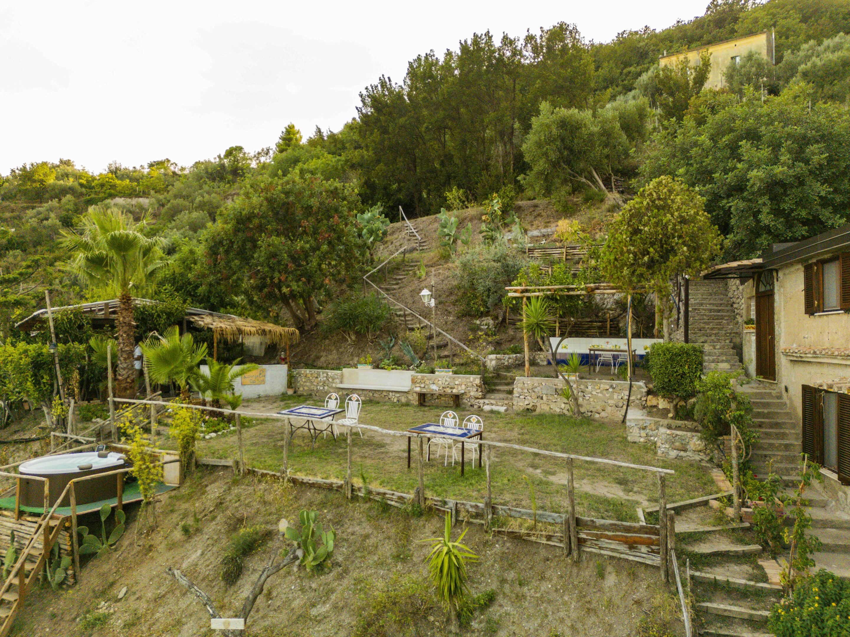 A rustic outdoor area with a hot tub, seating, and a staircase leading to a building.