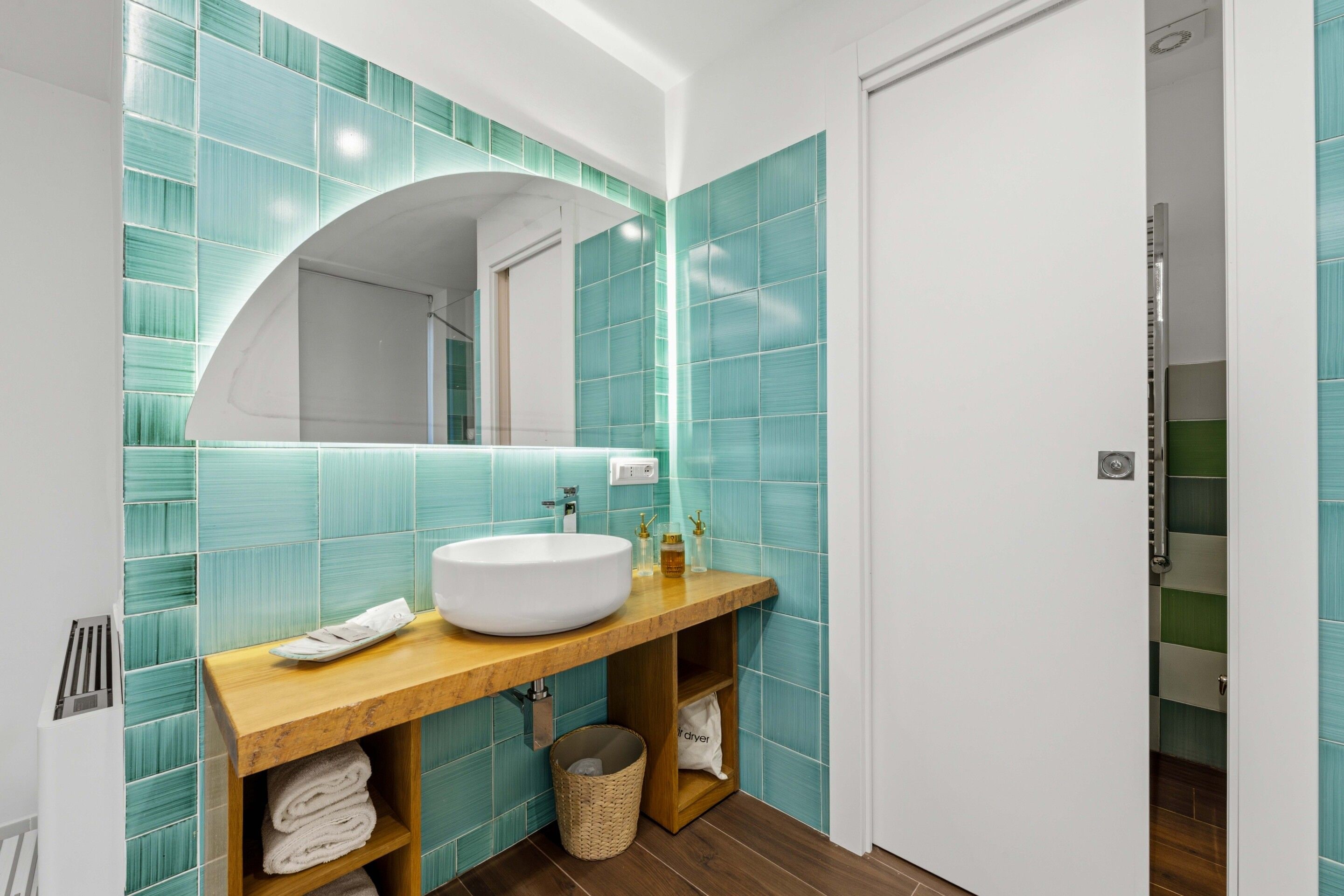 A bathroom with a white sink, a mirror, and teal tiles.