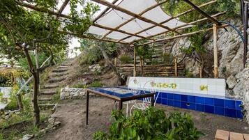 Un jardín al aire libre con una mesa y sillas, rodeado de plantas y un muro de piedra.