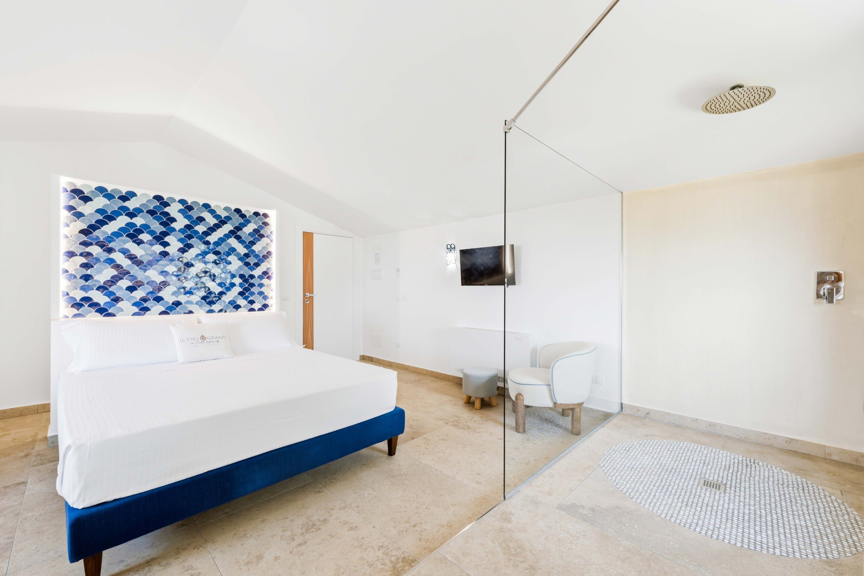 A modern bedroom with a large bed, a glass shower enclosure, a small desk, and a television mounted on the wall.