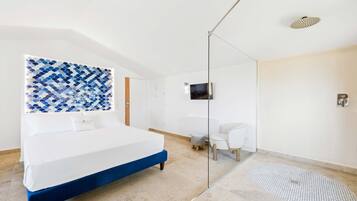 A modern bedroom with a large bed, a glass shower enclosure, a small desk, and a television mounted on the wall.