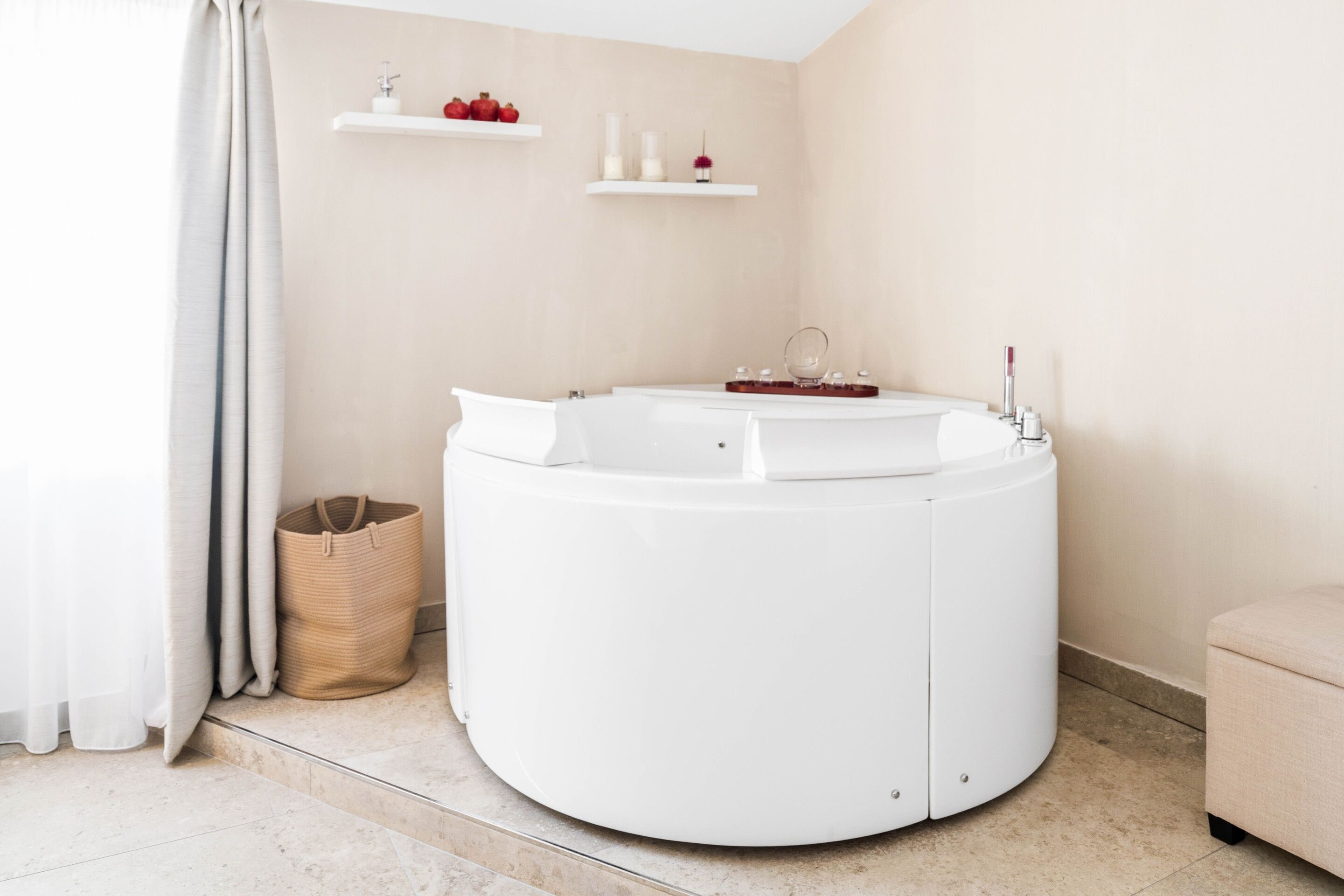 A modern bathroom with a freestanding bathtub, a small shelf with candles and a potted plant, and a wicker basket on the floor.