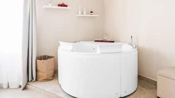 A modern bathroom with a freestanding bathtub, a small shelf with candles and a potted plant, and a wicker basket on the floor.