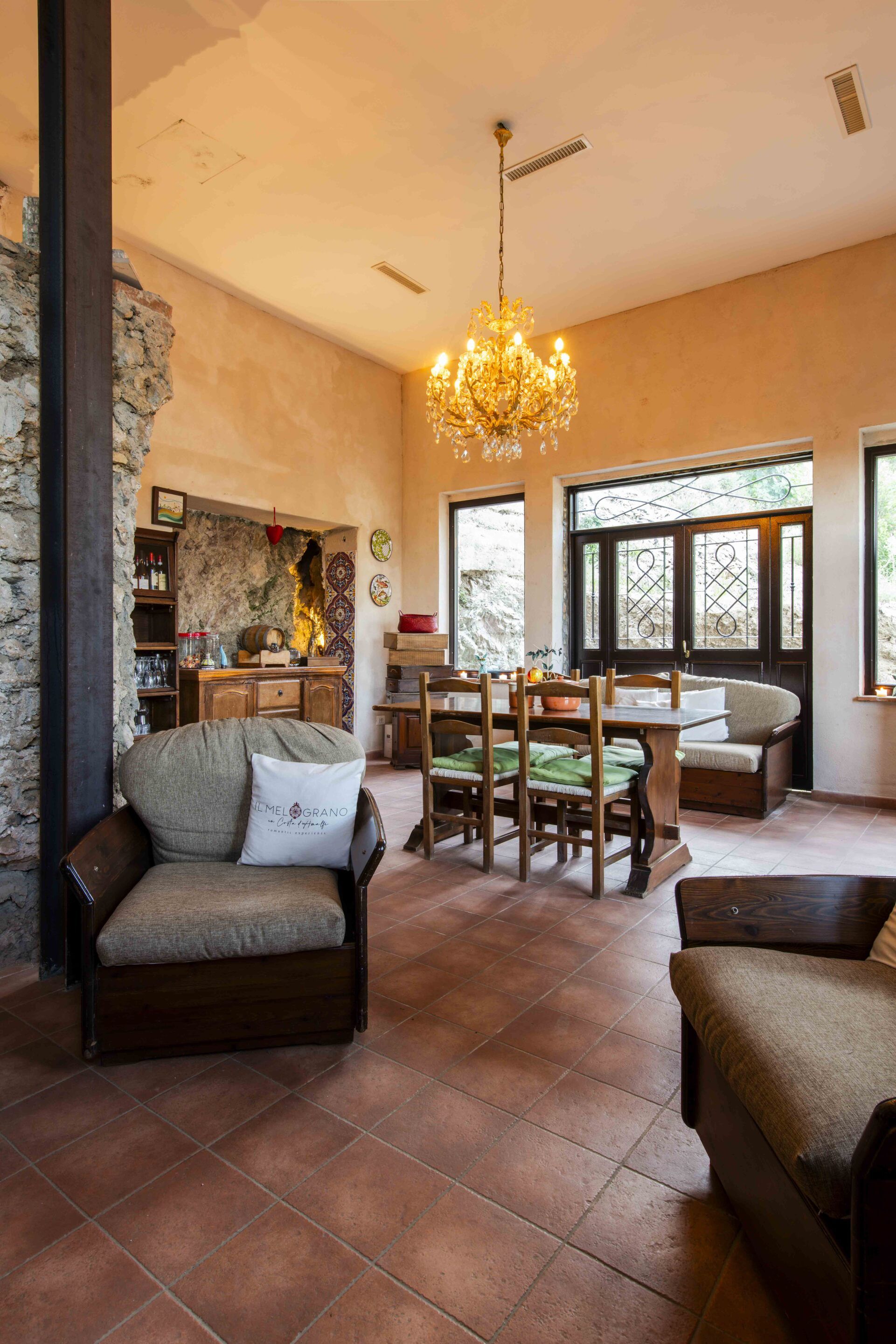 Amplia sala de estar con pared de piedra, candelabro y mesa de comedor con sillas.