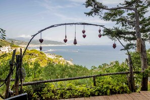 A view of a coastal landscape with a wooden archway adorned with heart-shaped ornaments, leading to a lush green area with cacti and a clear view of the sea and distant hills. - Il Melograno in Costa d'Amalfi (Vietri sul Mare)