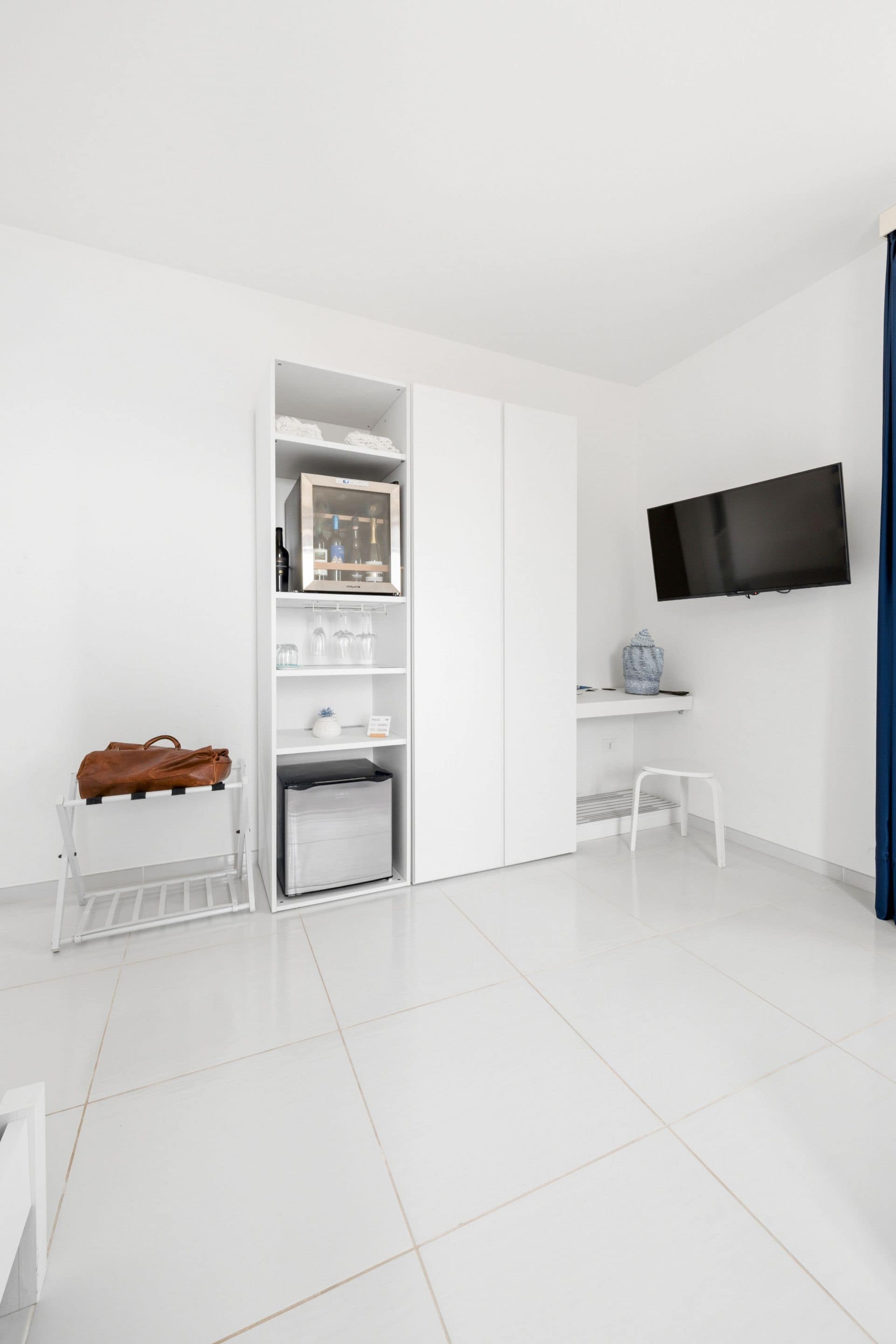 A modern, minimalist room with a white wardrobe, a flat-screen TV, and a small table.