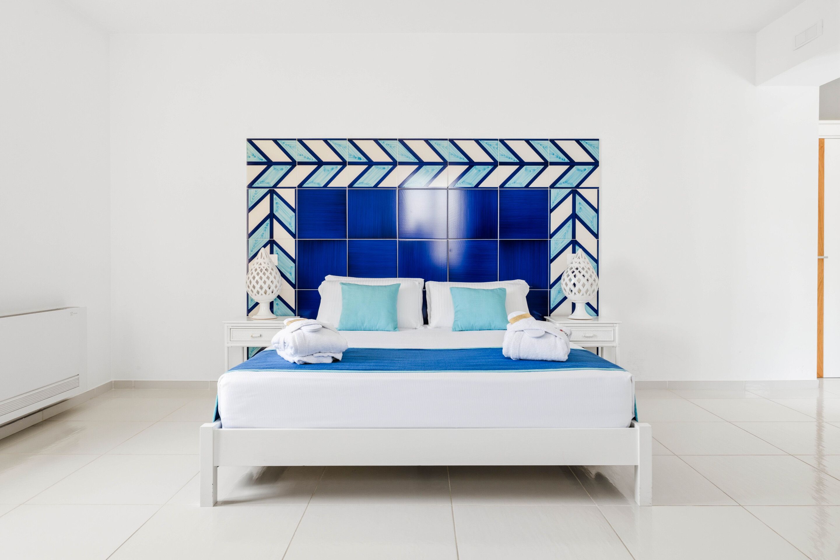 Una habitación de hotel moderna con una cama grande, cabecera blanca y una pared con estampado geométrico.