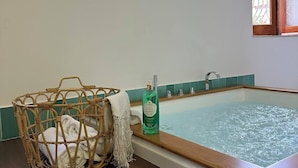 A bathroom with a wooden bathtub, a wicker basket with towels, and a bottle of Maison Royale Relaxant.