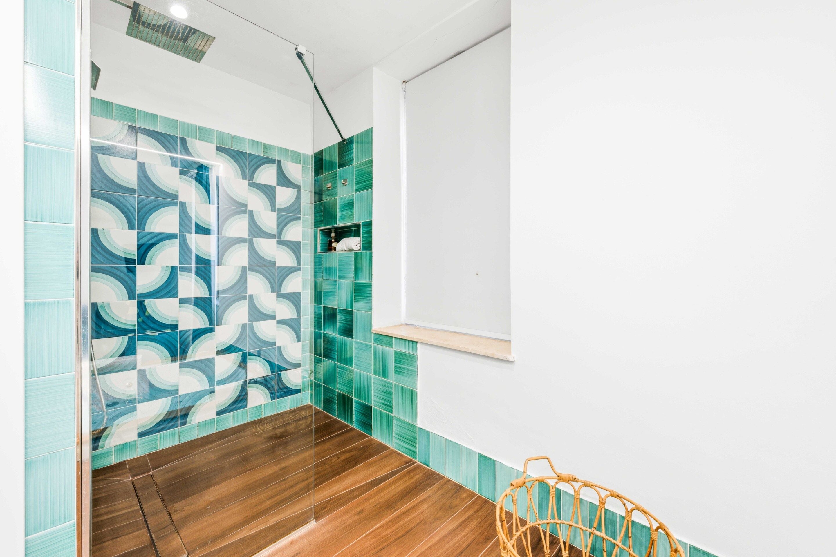 A bathroom with a shower area, a wooden floor, and a wall with a geometric tile pattern.