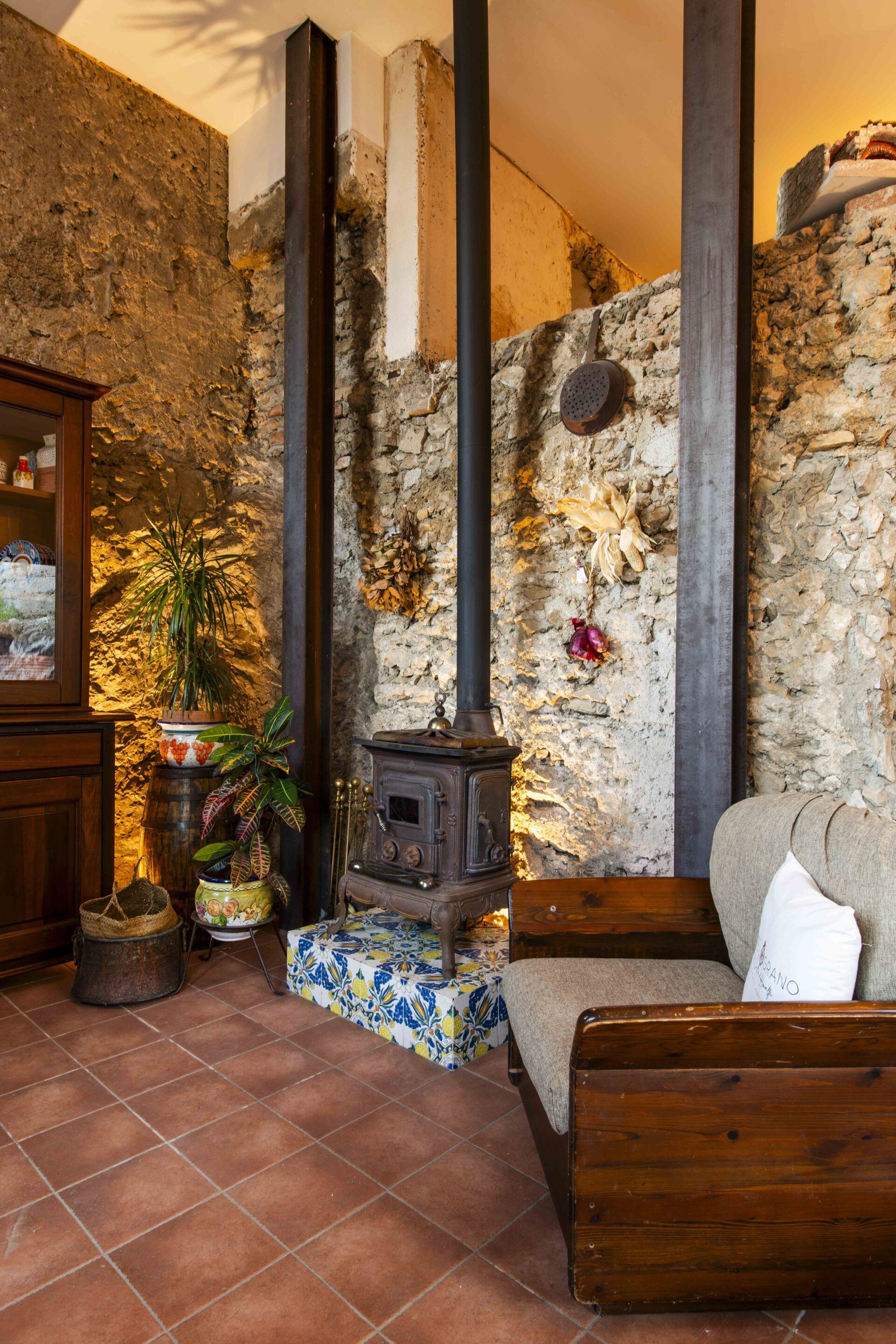 A rustic interior with a stone wall, a traditional wood-burning stove, a wooden cabinet, and a sofa.