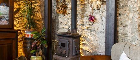 A rustic interior with a stone wall, a traditional wood-burning stove, a wooden cabinet, and a sofa.