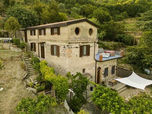 A rustic stone building with a balcony, surrounded by lush greenery.