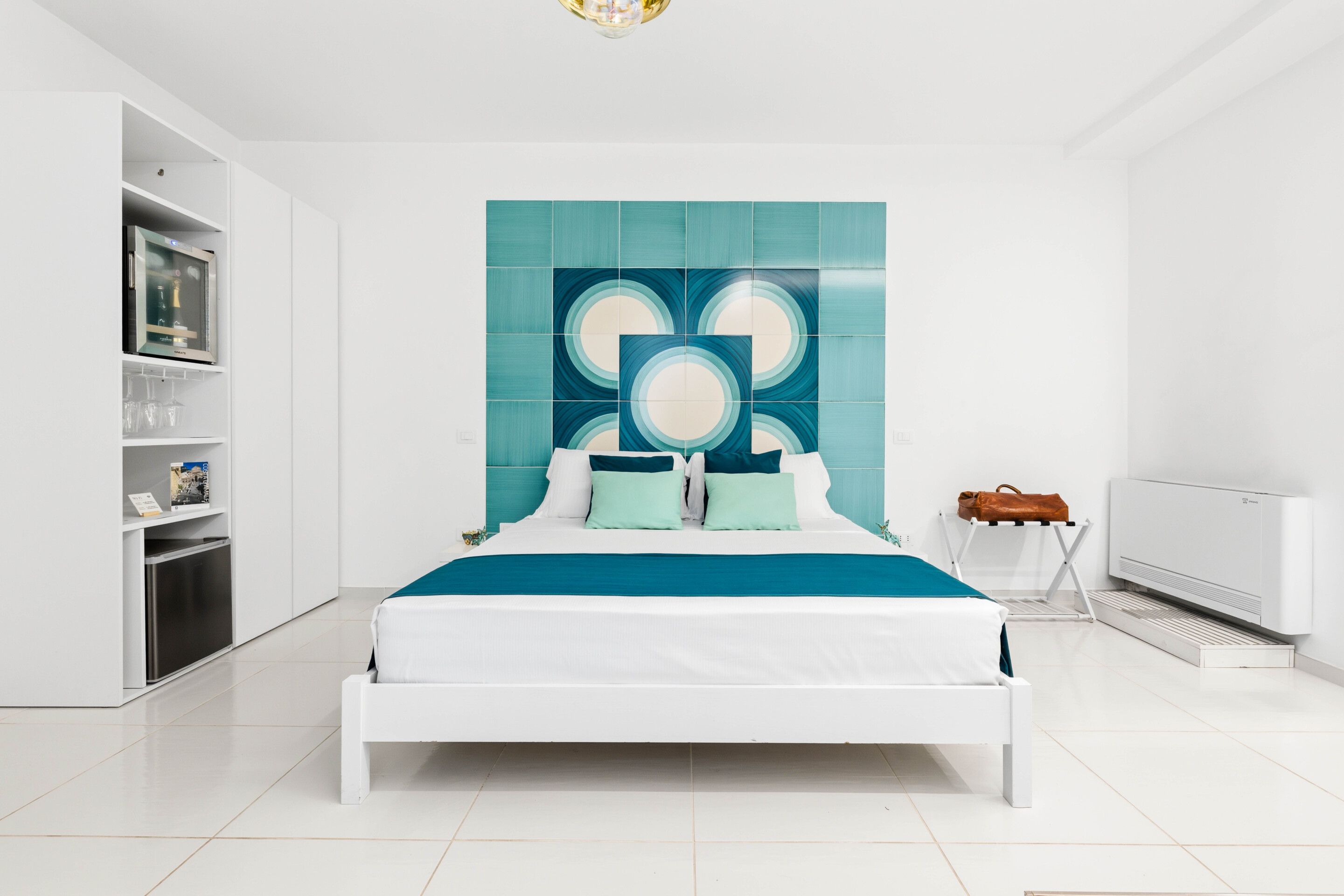 A modern bedroom with a white bed, teal accent wall, and built-in shelving.
