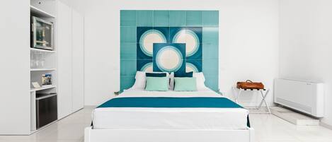 A modern bedroom with a white bed, teal accent wall, and built-in shelving.