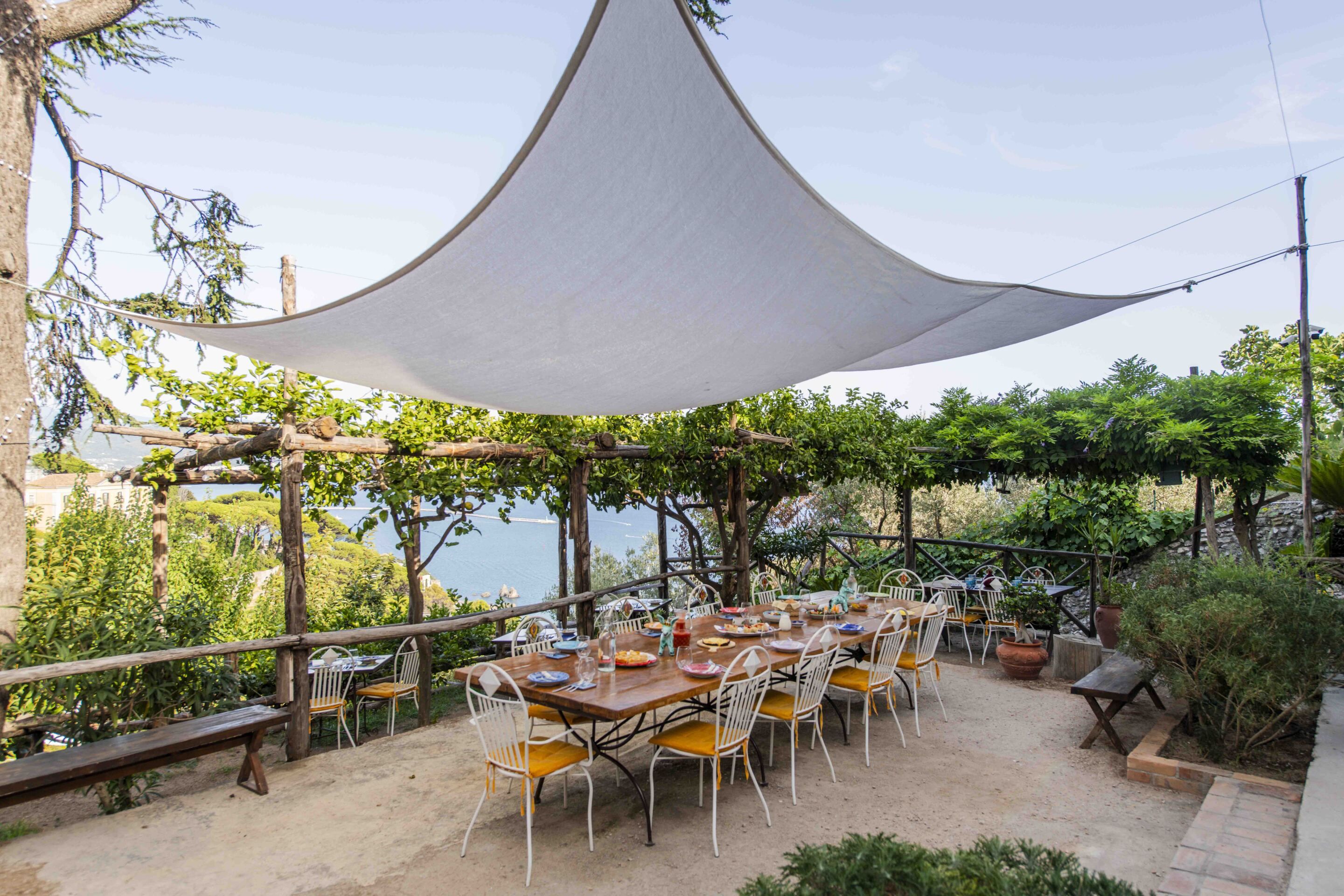Un espace de restauration en plein air, avec une table et des chaises placées sous un auvent, entouré de verdure et offrant une vue sur une étendue d’eau.