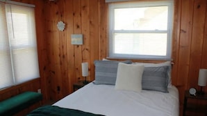 A wooden-paneled room with a bed, a bench, and a window. - Cozy little cottage in the heart of the Gem City (Quincy)