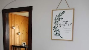 A dining area with a wooden table set for four, surrounded by black chairs. A framed sign with the word "gather" hangs on the wall. - Cozy little cottage in the heart of the Gem City (Quincy)