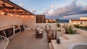 A rooftop terrace with wicker furniture, string lights, and a view of the sea. - Seaside Penthouse! Rooftop Jacuzzi & Ocean Views! (Tulum Municipality)