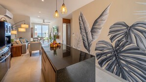 A modern kitchen with a central island, pendant lighting, and a large tropical leaf mural. - Seaside Penthouse! Rooftop Jacuzzi & Ocean Views! (Tulum Municipality)