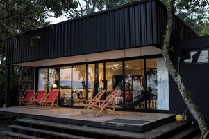 Un edificio moderno con un patio cubierto, que cuenta con varias sillas de madera y una pared de vidrio.
