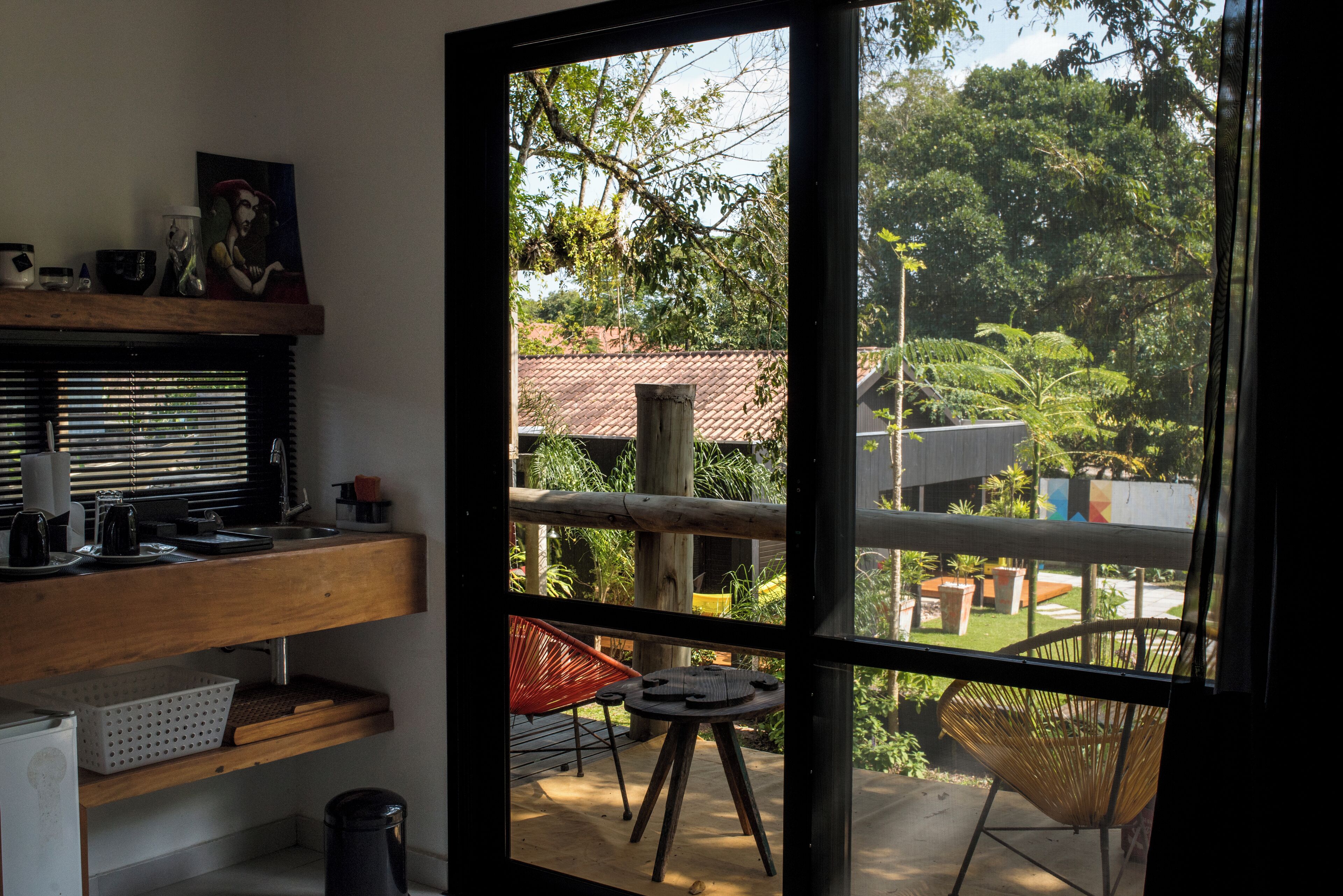 Ein Zimmer mit einer Holzhilfe, einem roten Stuhl und Blick auf einen Garten durch eine Glastür.