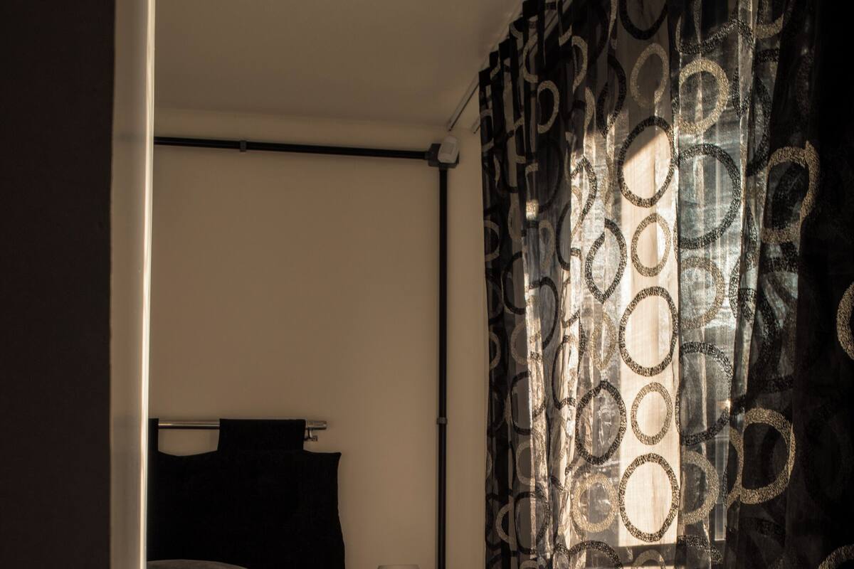 A bedroom with a bed, a nightstand, a lamp, and a window with curtains.