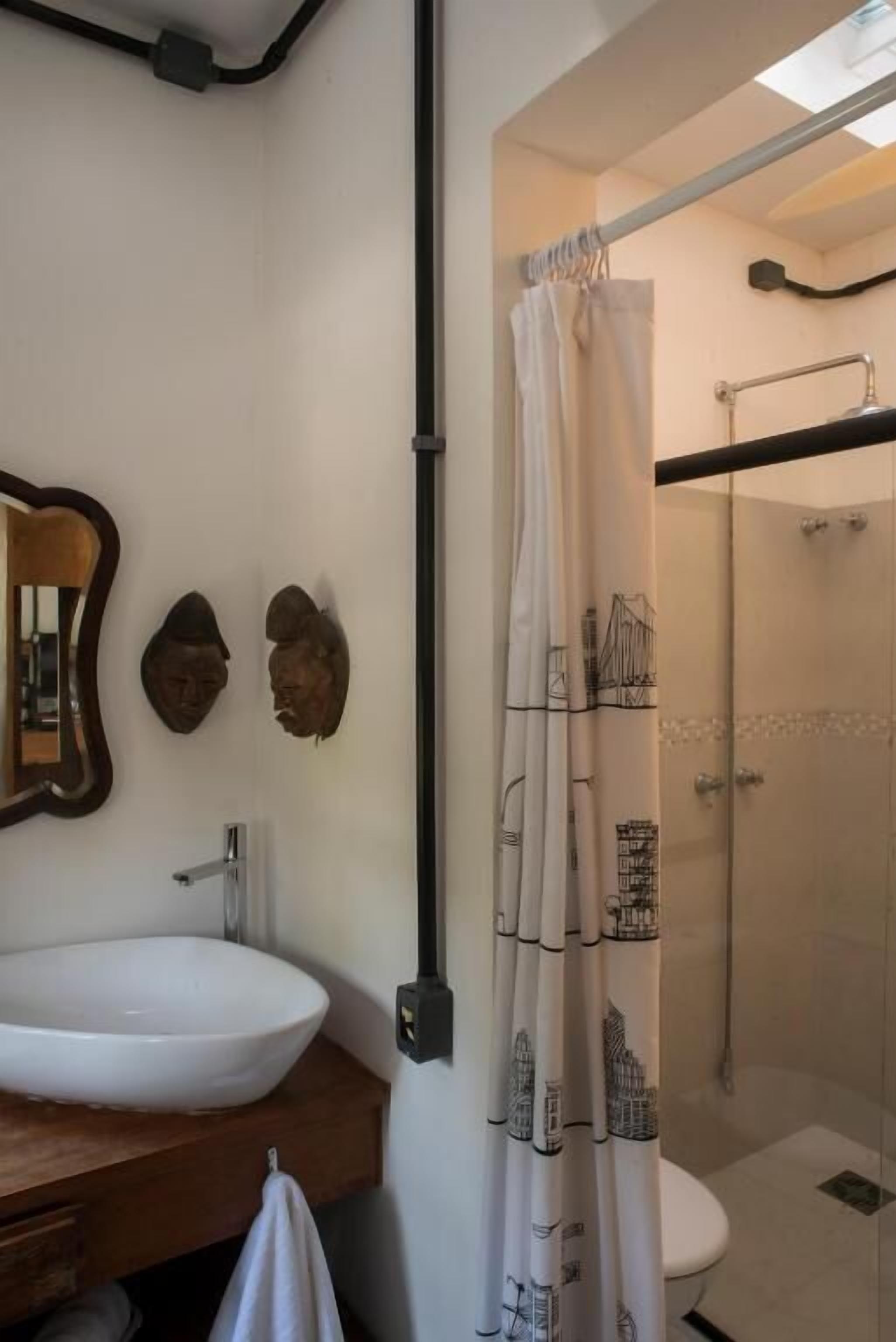 Un baño con un lavamanos blanco, un espejo y una ducha con cortina transparente.