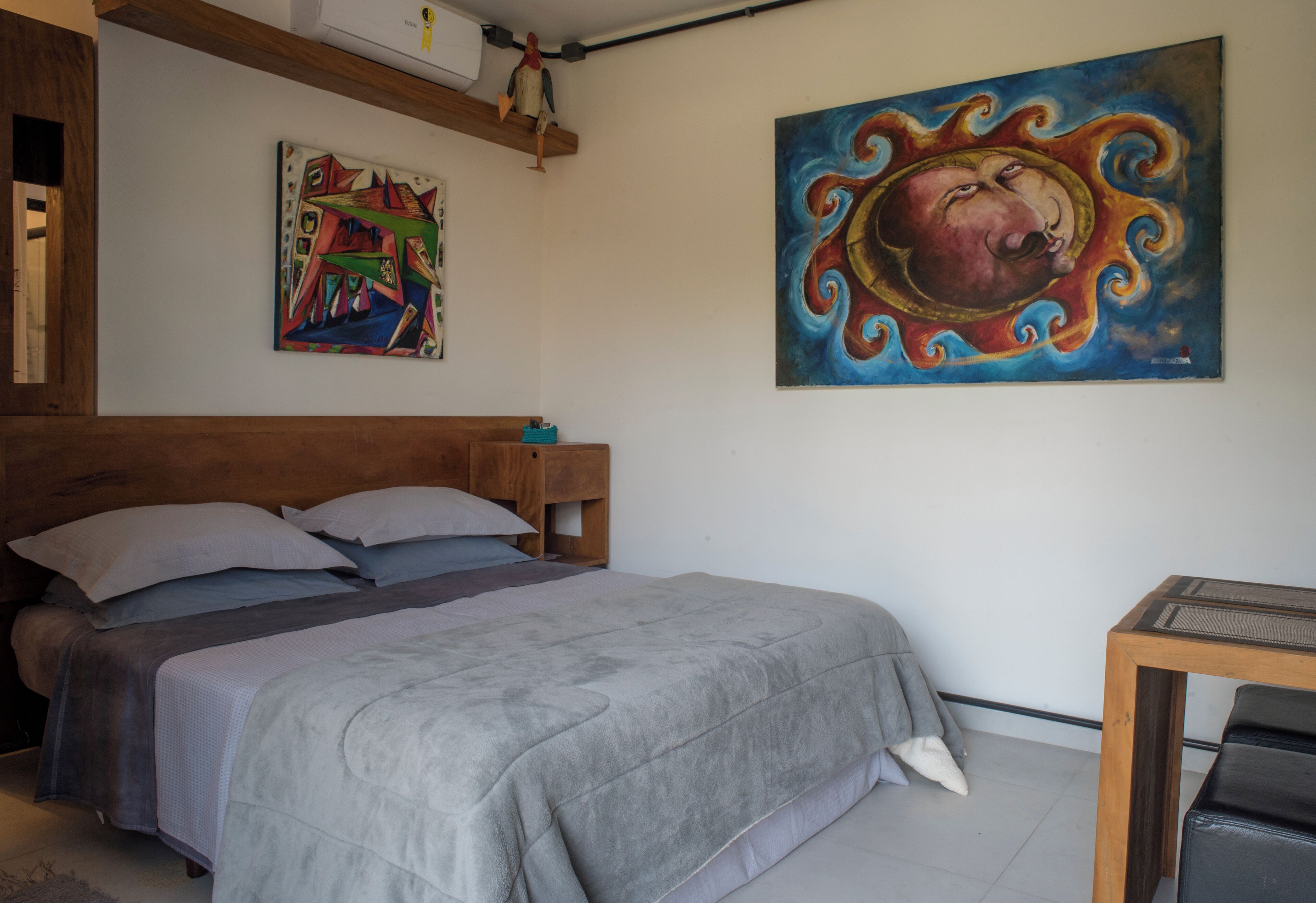 A bedroom with a bed, a wooden headboard, a painting on the wall, and a small table.