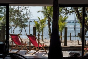 Una habitación con un ventanal que da a la playa, dos sillas rojas de playa y una mesa de madera.