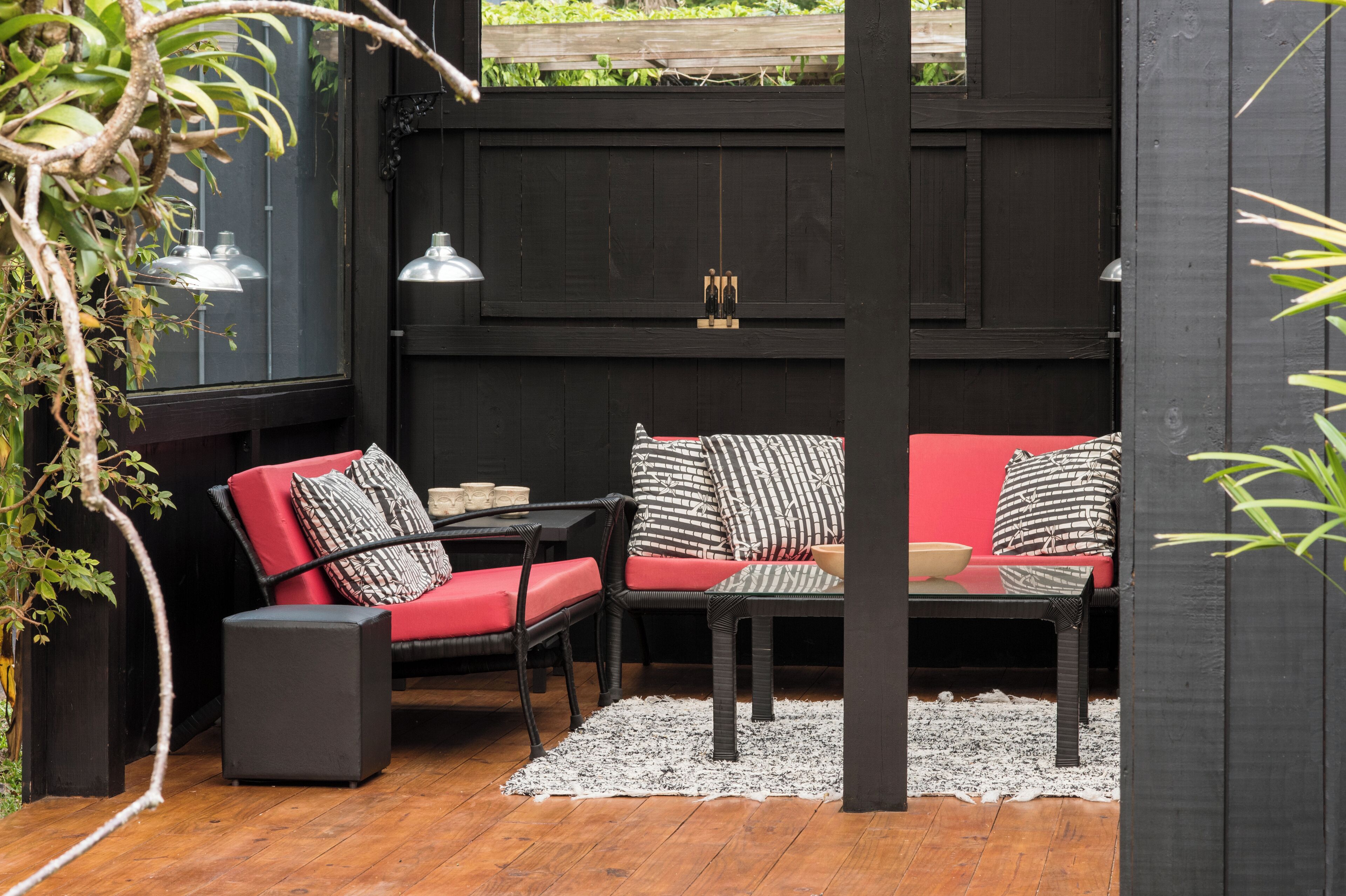 Un espacio al aire libre acogedor con un sofá rojo y dos sillones, una mesita y un altavoz.