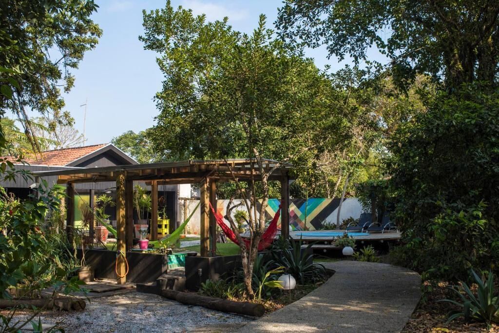 A covered outdoor area with a wooden structure, surrounded by lush greenery and a pool.